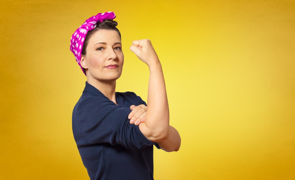 Es ist ein langer Weg von der Feminisierung des Berufsstands zur Repräsentanz von Frauen in der Standespolitik. Ein Bild, das eine Frau in blauem Hemd mit hoch gekrempelten Ärmel und einer Pink-weiß-gepunktetem Kopftuch vor gelbem Grund zeigt.