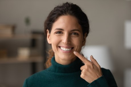 Ein Bild, das eine junge, lächelnde, dunkelhaarige Frau zeigt, die mit einem Finger ihrer Hand auf ihre Zähne zeigt