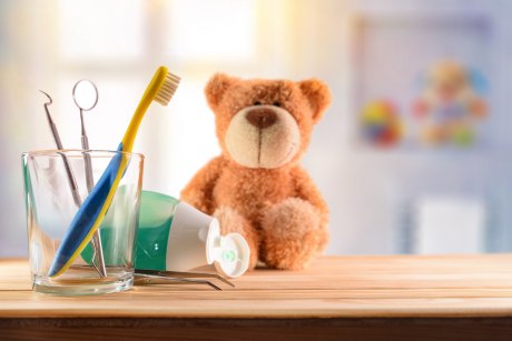Glas mit Zahnbürste und Zahnarzt-Instrumenten, daneben geöffnete Tube und Teddybär