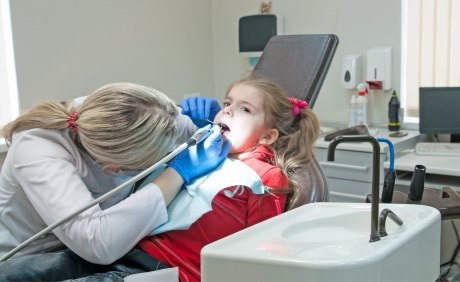 behandelnde Zahnärztin für Kind auf Behandlungsstuhl gebeugt